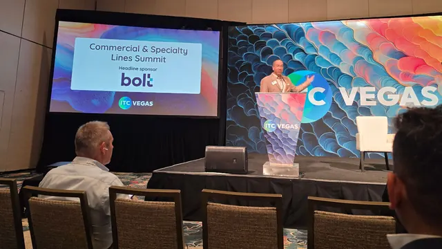 A speaker at the ITC Vegas podium opening the Commercial and Specialty Lines Summit, with the summit title slide on the screen beside him.