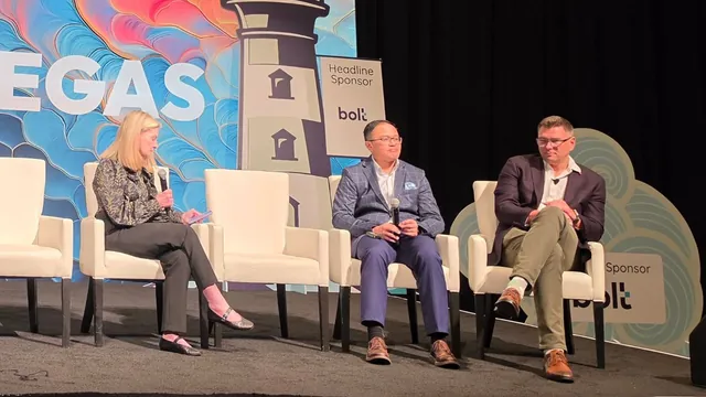 A moderator and two panelists seated on white chairs on the ITC Vegas stage, with the lighthouse backdrop and bolt headline sponsor signage behind them.