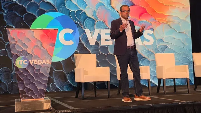 A presenter standing on the ITC Vegas stage, gesturing while speaking, with empty chairs behind.